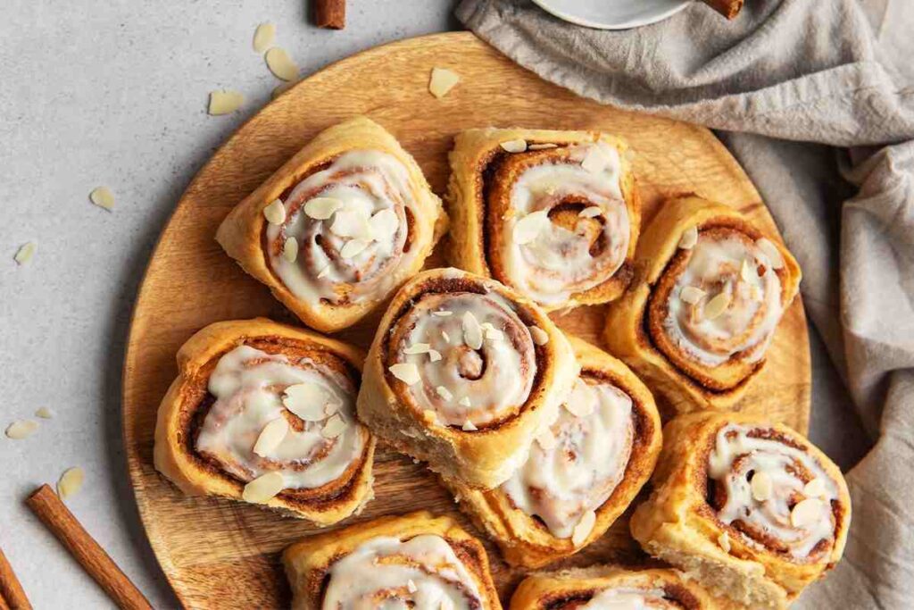 Zimtschnecken mit Zuckerguss und Mandelsplittern auf einem Holzbrett.