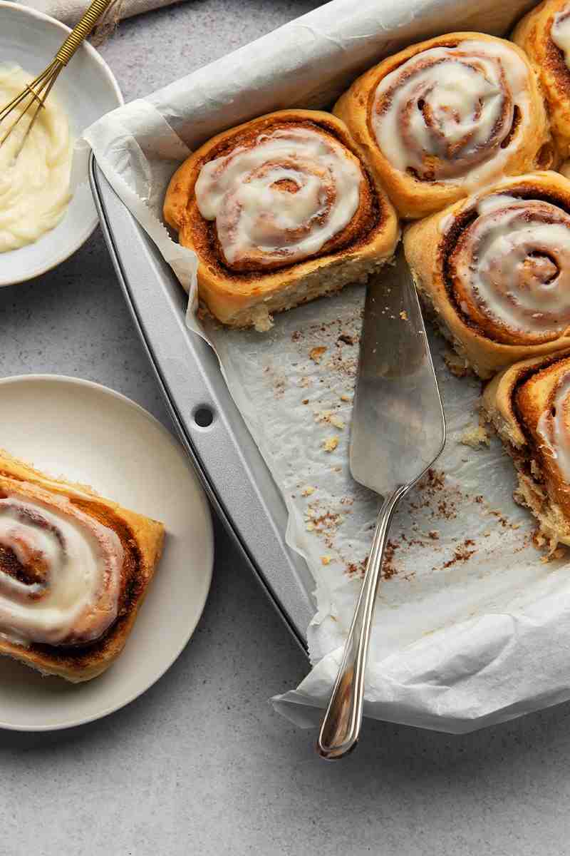 Zimtschnecken auf einem Holzbrett mit Zuckerguss und Mandeln