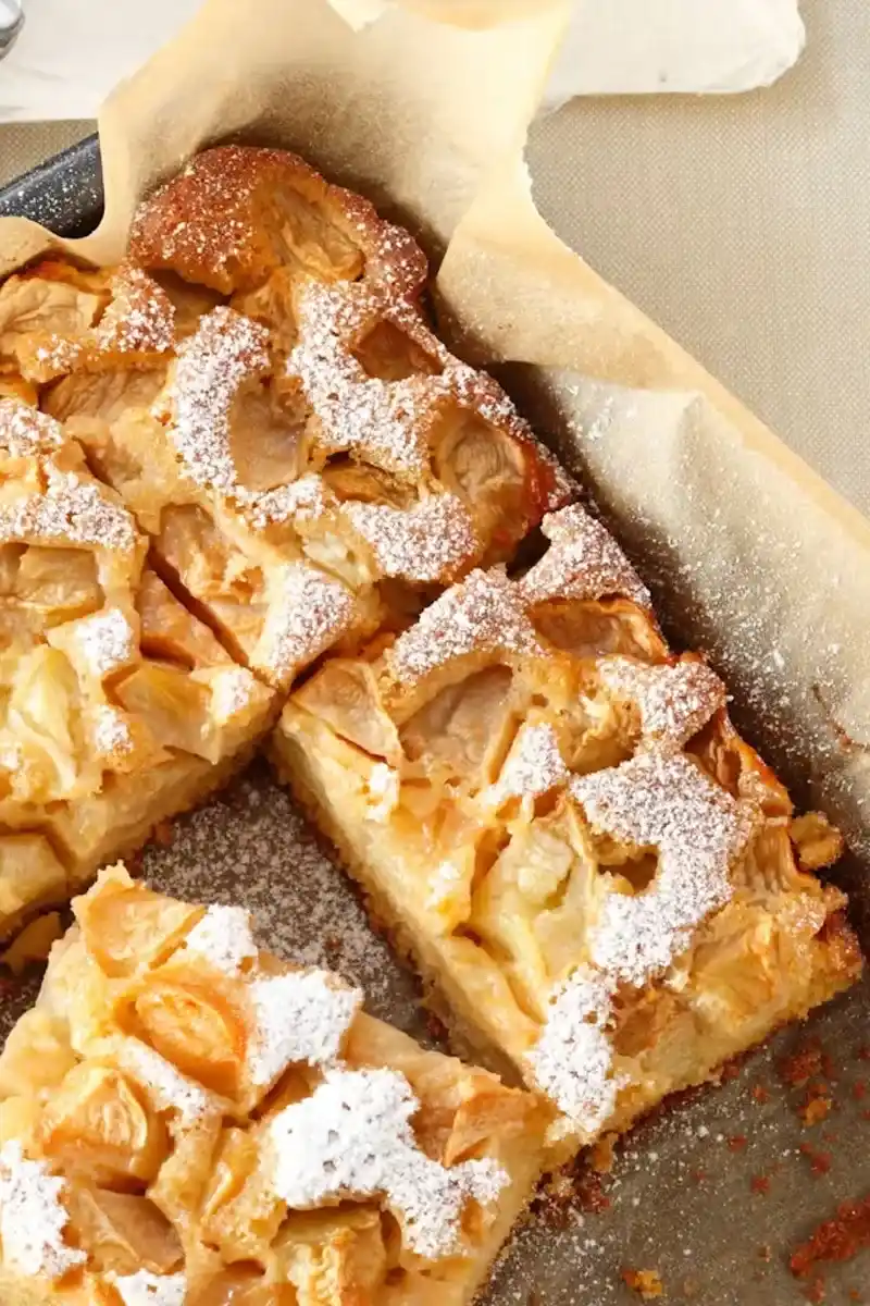 Ein ganzer Apfelkuchen in der Backform, gebacken nach einem einfachen apfelkuchen rezept, in Stücke geschnitten und mit Puderzucker bestäubt.