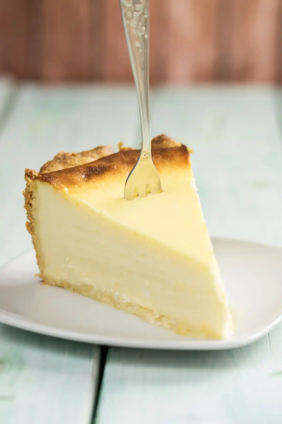 Nahaufnahme eines cremigen Stücks Käsekuchen Rezept auf einem weißen Teller, in das eine Gabel gesteckt ist