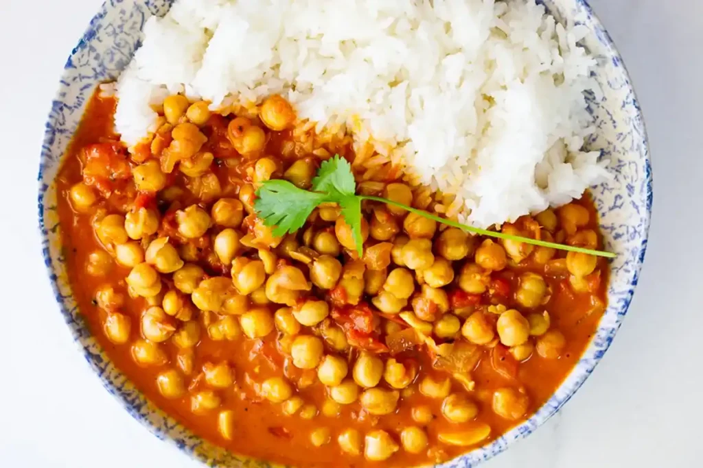 Eine Schüssel mit fertigem Kichererbsen Curry, serviert mit weißem Reis und garniert mit einem frischen Korianderzweig