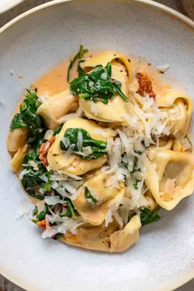 Nahaufnahme von einem Teller mit cremigen Tortellini, Spinat und frisch geriebenem Parmesan.
