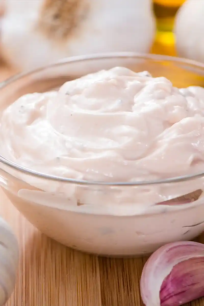 Nahaufnahme von cremiger, selbstgemachter Knoblauch-Mayonnaise nach einem einfachen Aioli Rezept in einer Glasschale.