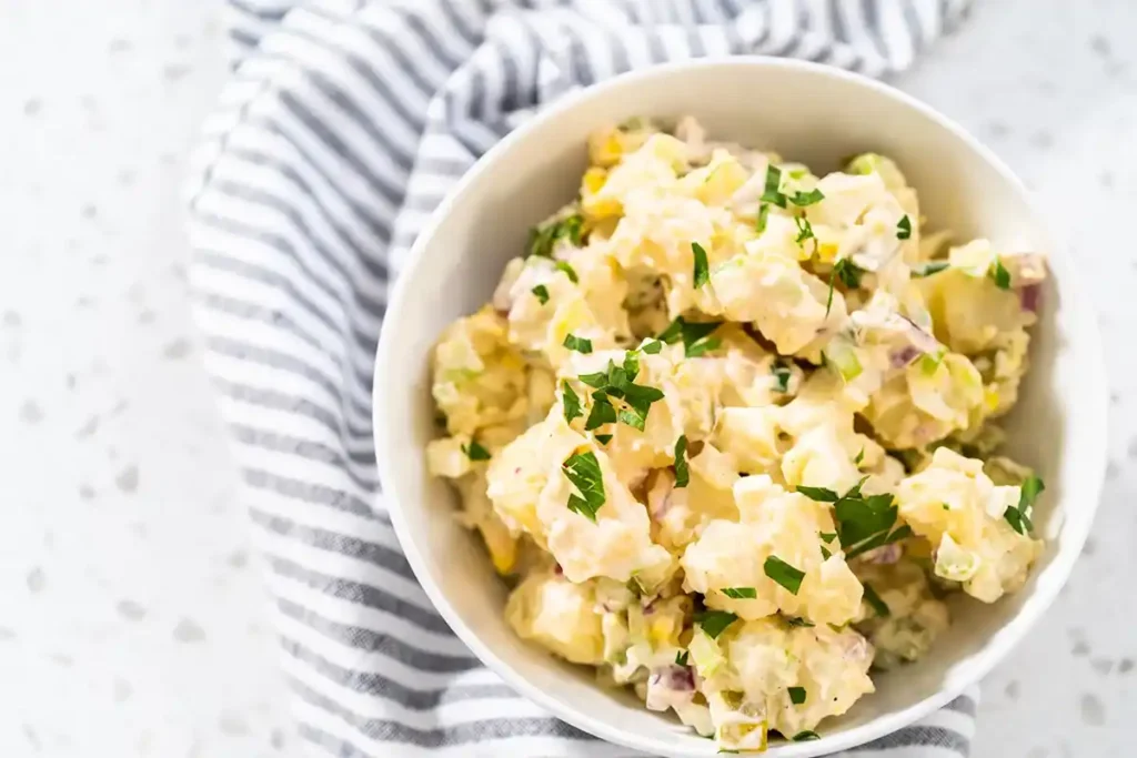 Cremiger Kartoffelsalat in einer Schale neben einem gestreiften Küchentuch