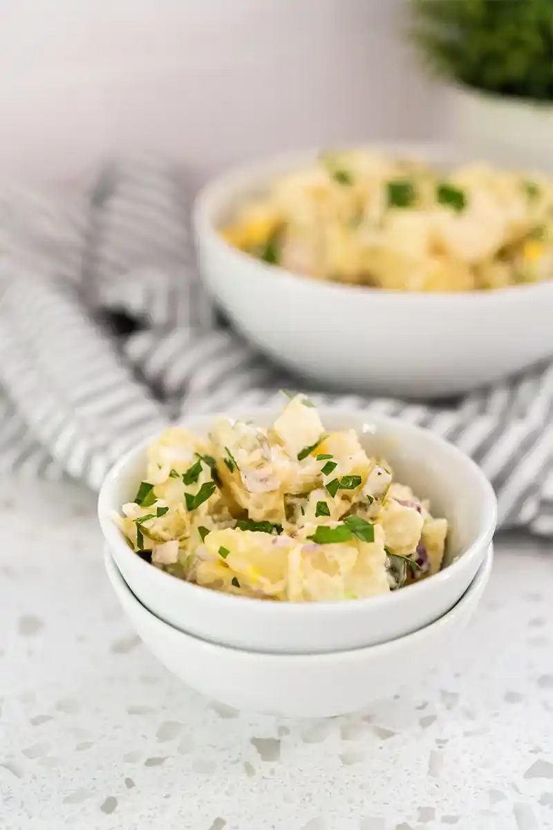 Zwei Schalen mit cremigem Kartoffelsalat, gestapelt auf einem hellen Hintergrund