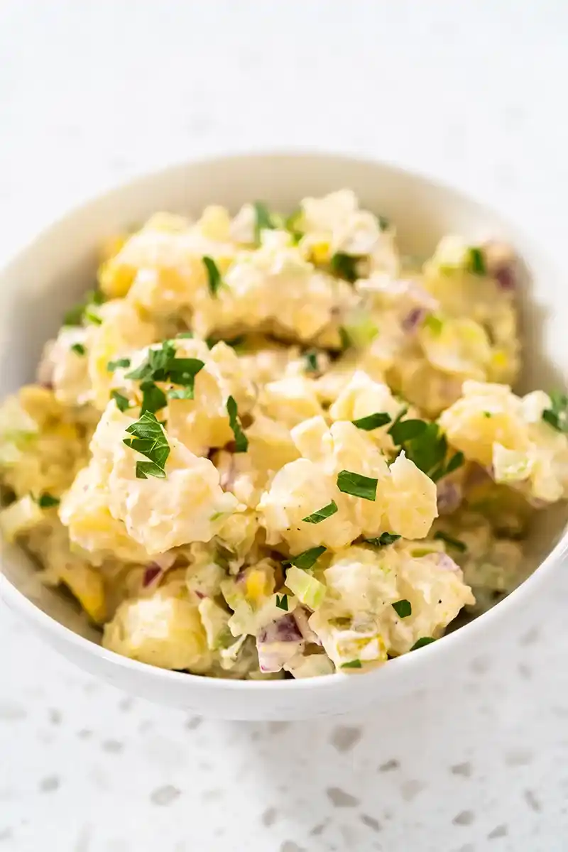 Cremiger Kartoffelsalat mit frischen Kräutern in einer weißen Schale.